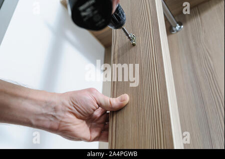 A man is installing a hook for clothes. He is using a screwdriver to fix the bracket hook. Stock Photo
