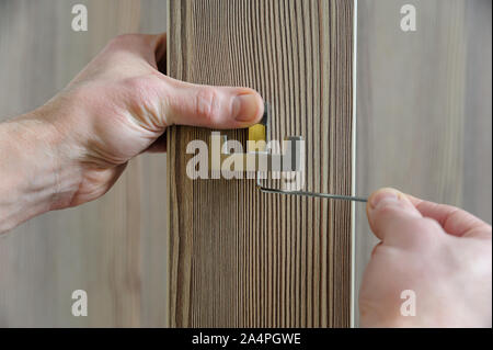 A man is installing a hook for clothes. He is using a hex key to fix the bracket of the hook. Stock Photo