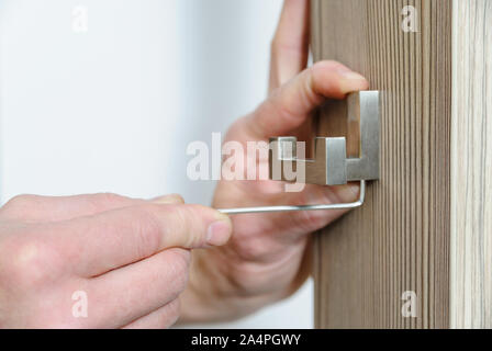 A man is installing a hook for clothes. He is using a hex key to fix the bracket of the hook. Stock Photo