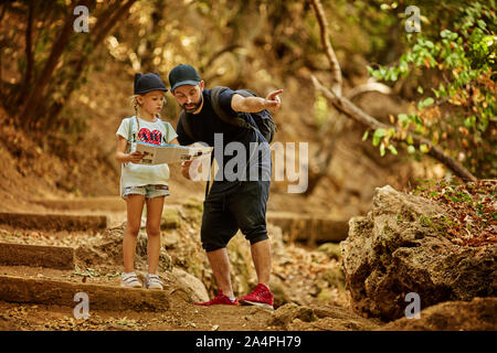 pretty family dad and little cute daughter hiking in a forest, looking at a map and pointing with hand. Stock Photo
