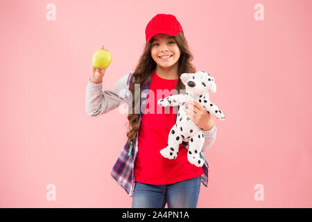 Apple is the happiest vitamin. Happy little girl hold apple and toy on pink background. Small child with healthy apple snack. Eating apple fruit full of vitamin is healthy for learn and play. Stock Photo