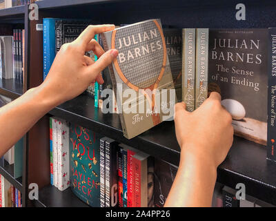 Man looking through books at a library or a book store. Hands holding a book with bookshelves in background, San Diego, USA, October, 09, 2019 Stock Photo