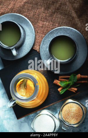 Transparent glass teapot with chitrus tea and cups, tea set on a wooden table. Close up, gray background, soft light Stock Photo