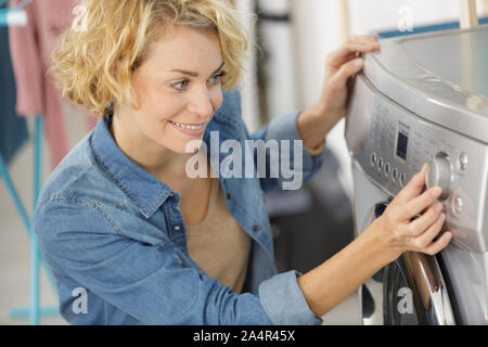 happy young woman turning regulator on washing machine Stock Photo