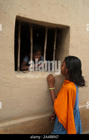 A cheerful girl from the Santal community talks to her friend, from the window of her home, in Joypurhat, Rajshahi, Bangladesh. May 20, 2011..The Santals are an ethnic minority community living in different districts of Rajshahi division in Bangladesh.  Most do not own land and work as daily paid labourers for very low wages. Much of the advancements in technology have bypassed these isolated communities where males dominate and women shoulder the burden of farming and carrying out other livelihoods..Santals are also the largest ethnic group in India where they have settlements in the states o Stock Photo