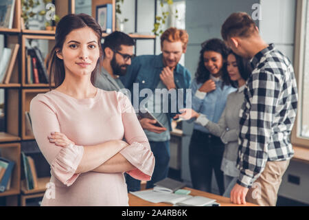 Startupers working together at office pregnant woman close-up crossed arms looking camera serious while colleagues using digital tablet Stock Photo