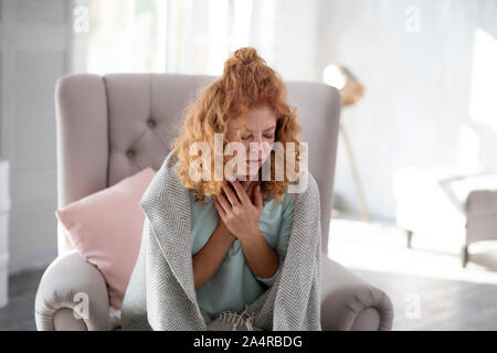 Woman coughing while sitting on armchair having sick leave Stock Photo