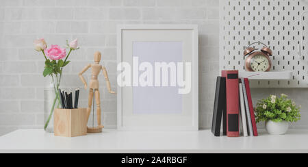 Minimal workplace with mock up frame, books and decorations on white table and grey brick wall background Stock Photo