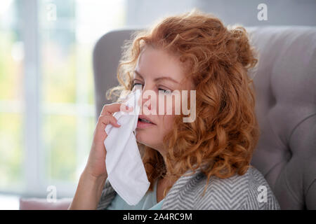 Woman holding napkin while sneezing and feeling dizzy