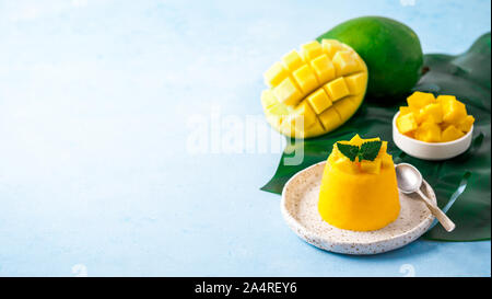 Mango Mousse on blue background with copy space left. Yellow mango mousse with sliced ripe mangoes. Banner. Stock Photo