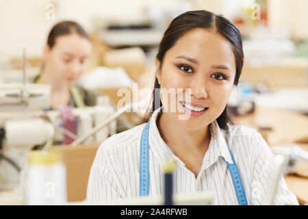 Portrait of Asian young seamstress smiling at camera while working at her workplace in workshop Stock Photo