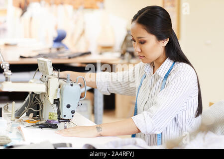 Asian young designer concentrating on her work she sitting at the table and using sewing machine in her work Stock Photo