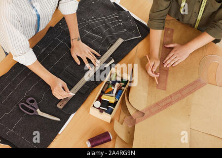 Close-up of two tailors drawing patterns and working with fabrics in team at the table in workshop Stock Photo