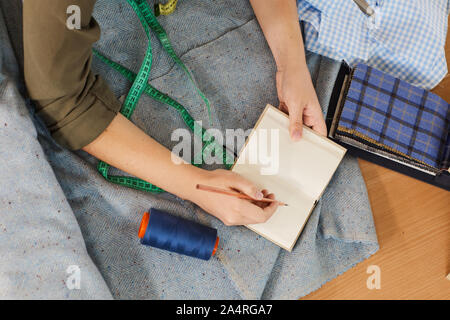 Close-up of female student opening her notepad and making notes during sewing lesson at the table in workshop Stock Photo