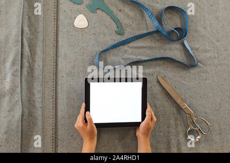 Close-up of tailor holding digital tablet and using it in her work while making pattern on fabric Stock Photo