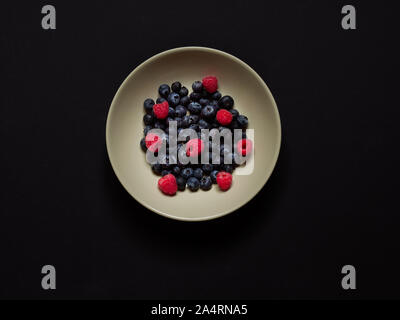 Blueberries and Raspberries in a cream dish on a black background in studio viewed from above, flatlay concept Stock Photo
