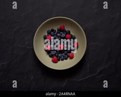 Blueberries and Raspberries in a cream dish on a black background in studio viewed from above, flatlay concept Stock Photo