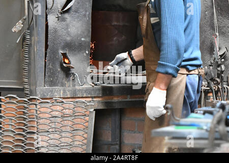 blacksmith heats iron in a furnace. young traditional Blacksmith working with open fire The blacksmith making flames in smithy with spark fireworks Stock Photo