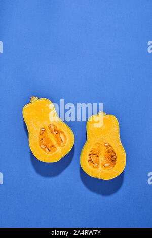 Two halves of ripe butternut squash pumpkin on a blue background. Orange pumpkin with a tail. Close-up Stock Photo