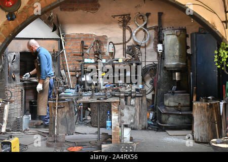 An experienced blacksmith works with open fire. A blacksmith extinguishes a flame in a forge with a spark firework, forges hot iron in a workshop Stock Photo