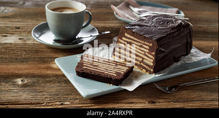 Close-up of a Kellerkuchen or Hedgehog slice chocolate cake served on blue ceramic tray and white paper, with cup of coffee on wooden table Stock Photo