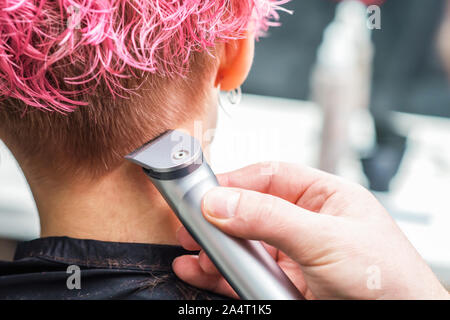 Close up hand of hairdresser shaves woman pink hair with electric shaver in beauty salon. Hands are shaving woman's hair. Stock Photo