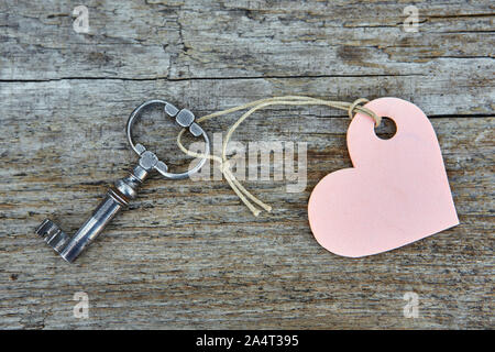 An antique handmade key with a heart-shaped label keychain lies on a wooden Board. Stock Photo
