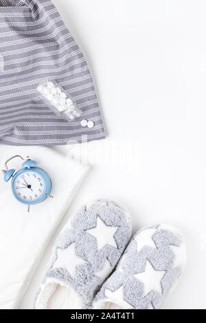 Sleep. Fluffy slippers, bottle with pills and blue alarm clock isolated on white background. Creative conceptual top view flat lay minimal style. Rest Stock Photo