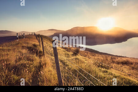 Misty summer sunrise over loch with reflection and barbed wire fence, Isle of Lewis, Outer Hebrides, Scotland Stock Photo