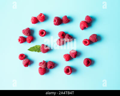 Pattern of ripe red raspberry on blue background. Creative layout of organic raspberries and green leaf. Top view or flat lay. Vegan food, detox concept Stock Photo