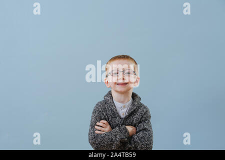 Funny little ginger boy in glasses holding hands crossed over blue background Stock Photo