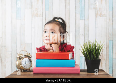 Cute little asian girl gazing and looking at empty space against books on table. Concept of education, future and daydreaming Stock Photo