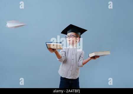 Redhead first grader boy in glasses and student hat looks at paper plane fly by Stock Photo