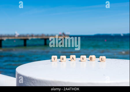 Word Travel on the background of the sea. Letters on wooden cubes on white and sand backgrounds. Stock Photo