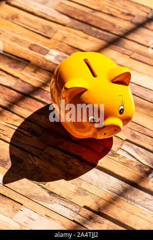 A yellow piggy bank stands on a wooden floor and casts a strong shadow Stock Photo