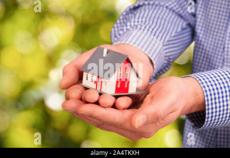 Hands carry a house in front of a green natural background with bokeh Stock Photo