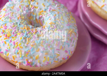 close up over head  image of a single donut with colorful sprinkles Pink background for copy space Stock Photo