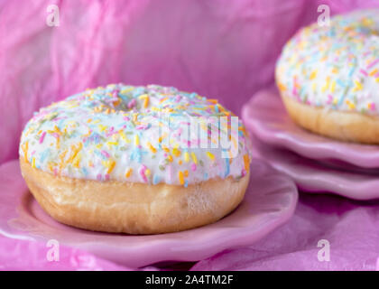 close up head on image of a single donut with colorful sprinkles Pink background for copy space Stock Photo