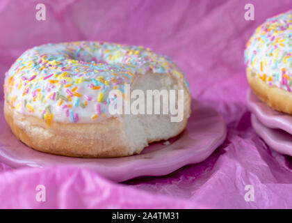 head on image  colorful sprinkles doughtnut   on a plate with a bite taken out Pink background for copy space Stock Photo