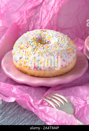 vertical image of a single donut with colorful sprinkles Pink background for copy space Stock Photo