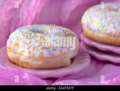close up head on image of a single donut with colorful sprinkles with a bite taken out Pink background for copy space Stock Photo