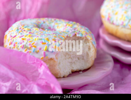 head on image  colorful sprinkles doughtnut   on a plate with a bite taken out Pink tissue paper  background for copy space Stock Photo