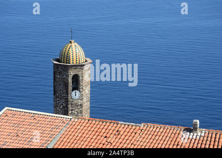 the bell tower of the Cathedral of Sant'Antonio Abate, which emerges beyond the roof of a house, in the ancient village of Castelsardo Stock Photo