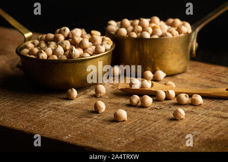 Raw chickpeas in spoons on a wooden kitchen board on a dark background Stock Photo