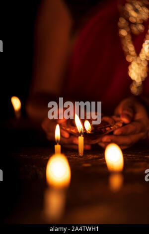 Indian housewife wearing traditional jewelery & lighting candles with diya or clay lamp on Diwali festive holiday season. Background for dhanteras, in Stock Photo