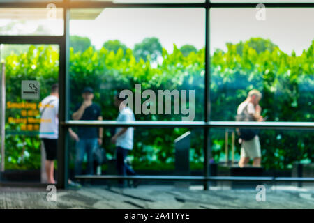 Blurred people smoking in smoking zone area of the mall or office. Four man smoke in smoking area beside green wall of tree. Quit smoke or smoking Stock Photo