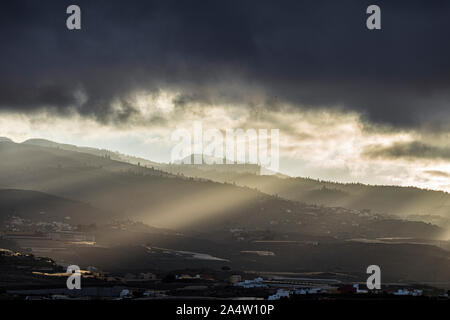 Early morning sunlight breaks through the clouds over the mountains sending rays of light on to the land below, Guia de Isora, Tenerife, Canary Island Stock Photo