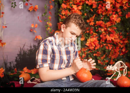 Photo of angry young man on halloween wearing classical plaid shirt holding orange pumpkin over street background with autumn leaves. Stock Photo
