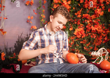 Photo of angry young man on halloween wearing classical plaid shirt holding orange pumpkin over street background with autumn leaves. Stock Photo