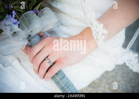 Bride shows off wedding ring, purple bouquet, veil and white wedding dress Stock Photo